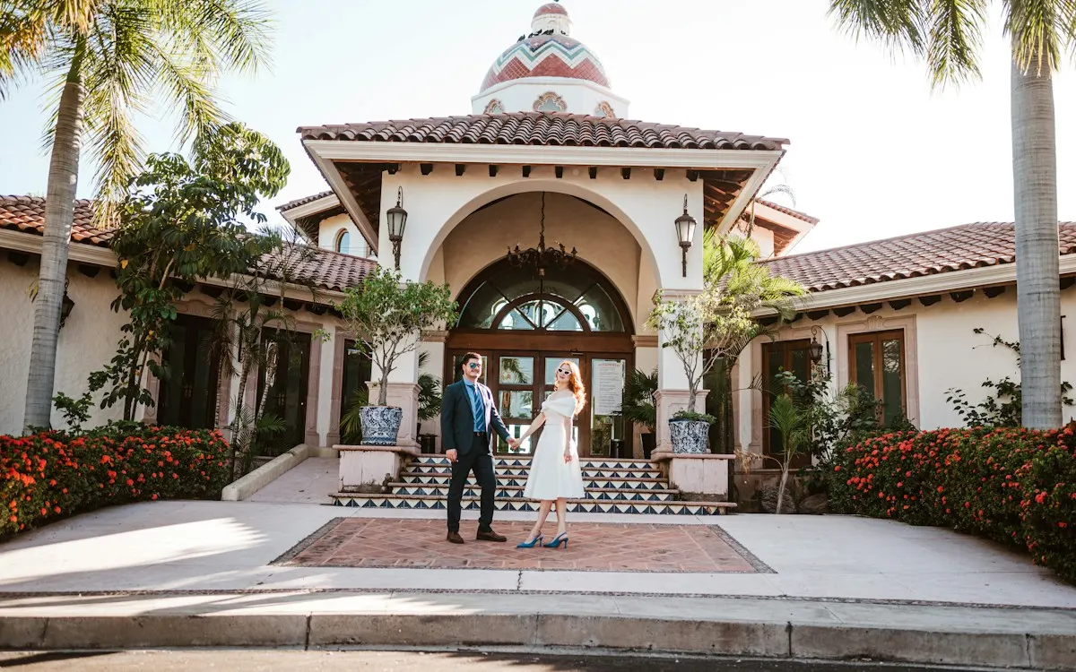 Newly married couple holding hands in front of a whitewashed building with a tiled dome