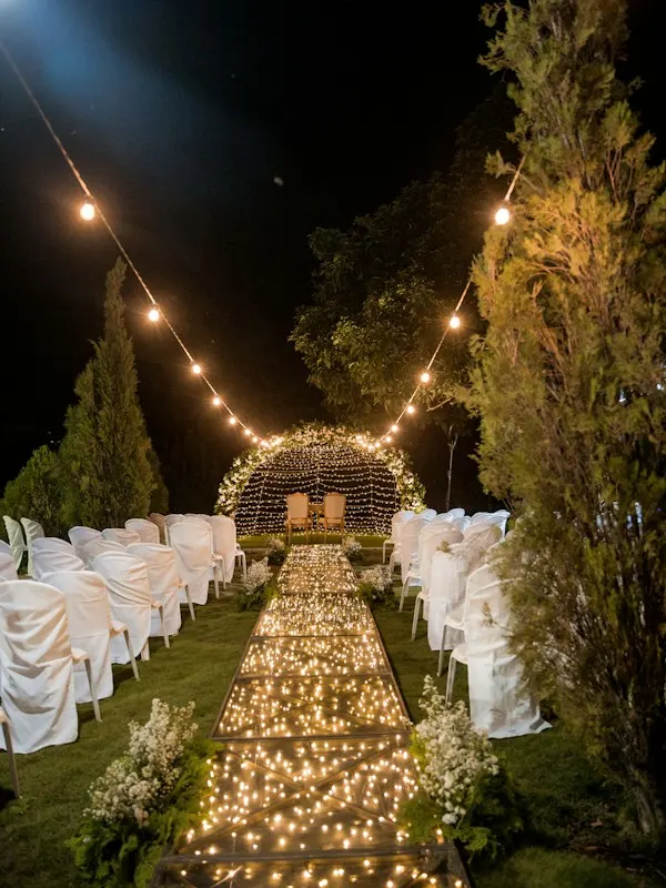 Outdoor wedding aisle lined with candles and string lights at night